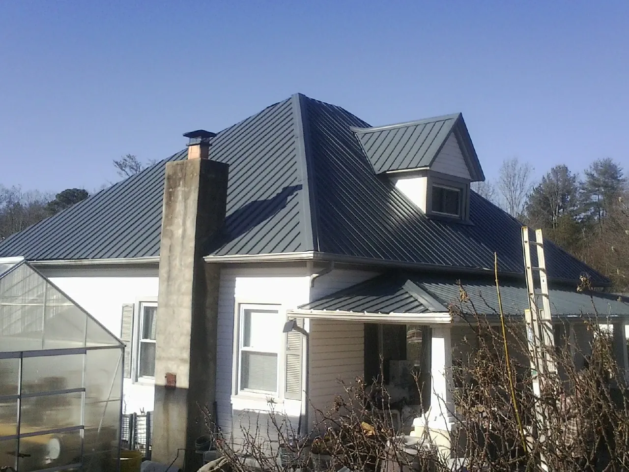 Dark blue standing seam metal roof on a white farmhouse with dormer — Slate & Tile Roof Repair by Roofing Brothers in Pavo
