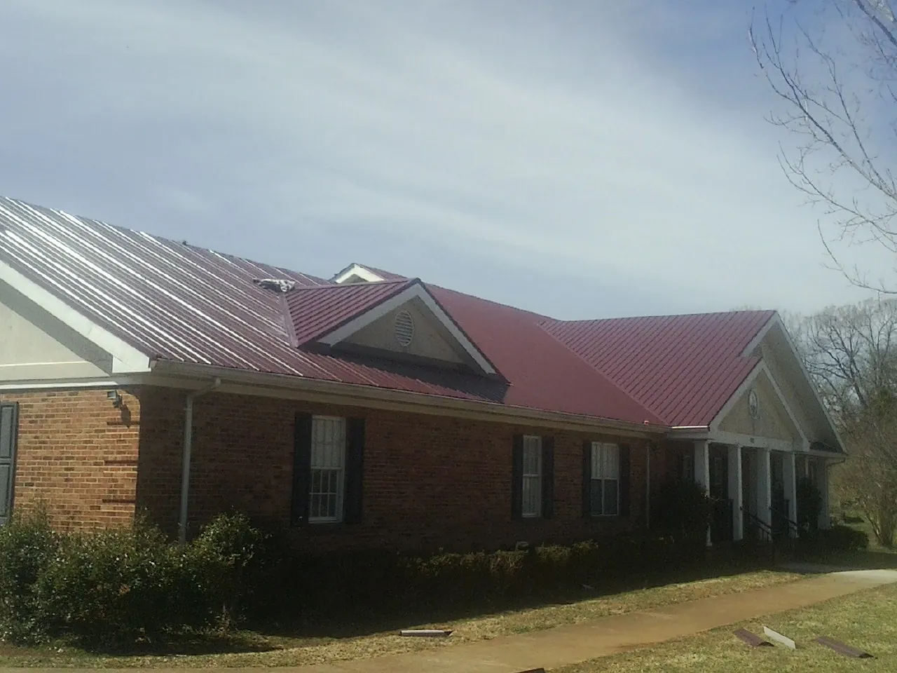 Red metal roof with gabled entries on a long brick building, from a Hail Damage Roof Repair job in Pavo