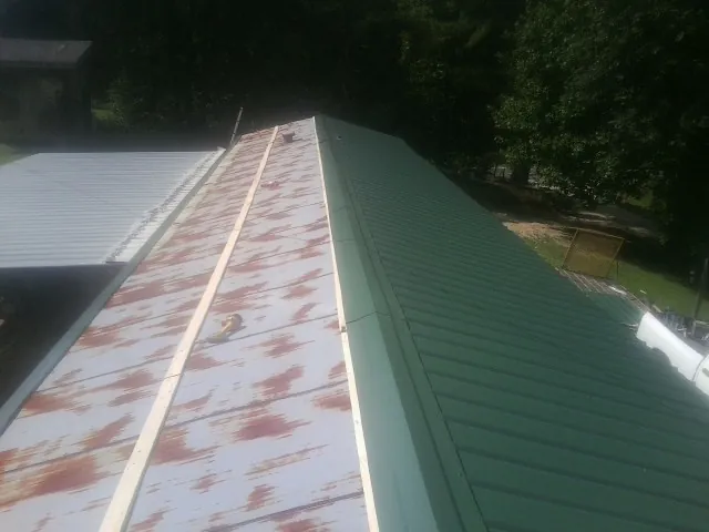 Old rusted panels beside newly installed green metal roofing — Wind Damage Roof Repair by Roofing Brothers in Pavo