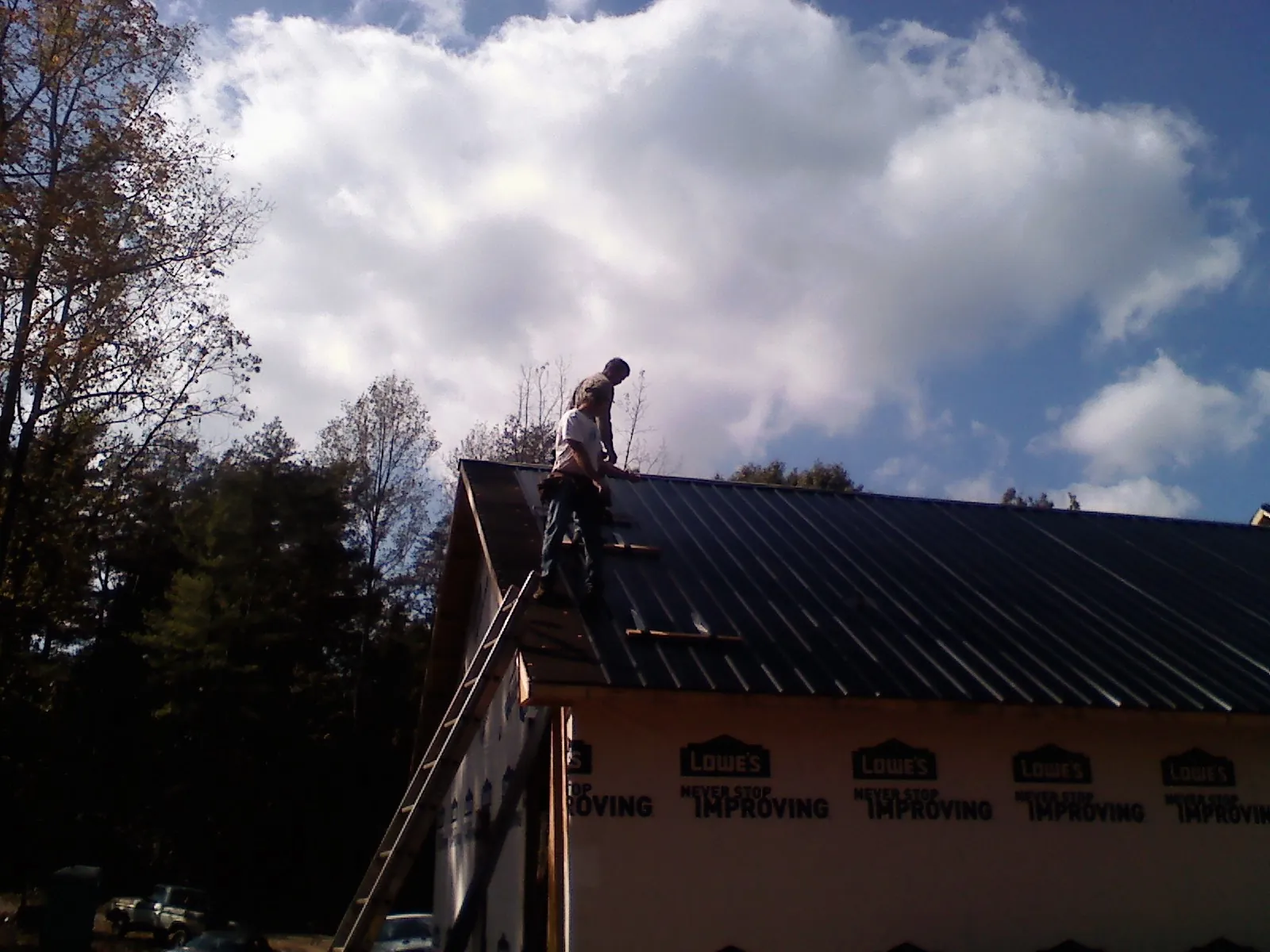 Roofer fastening dark metal panels high against a cloudy sky, from a Roof Inspection job in Pavo