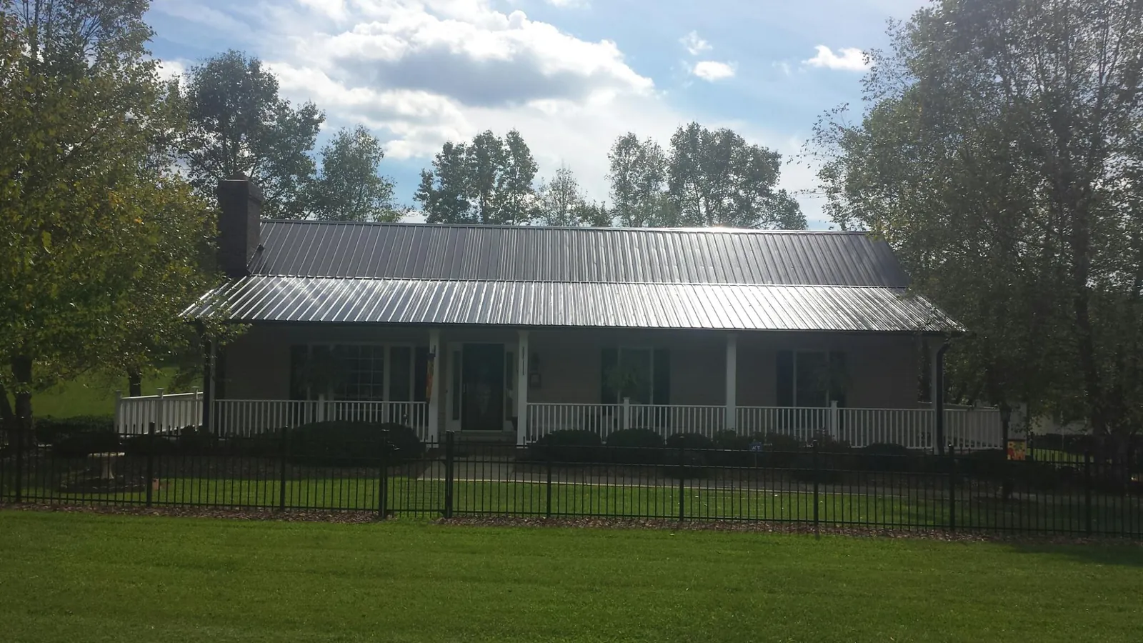 Gray metal roof on a brick ranch with a full width front porch — Gutter Guard Installation work by our crew in Pavo