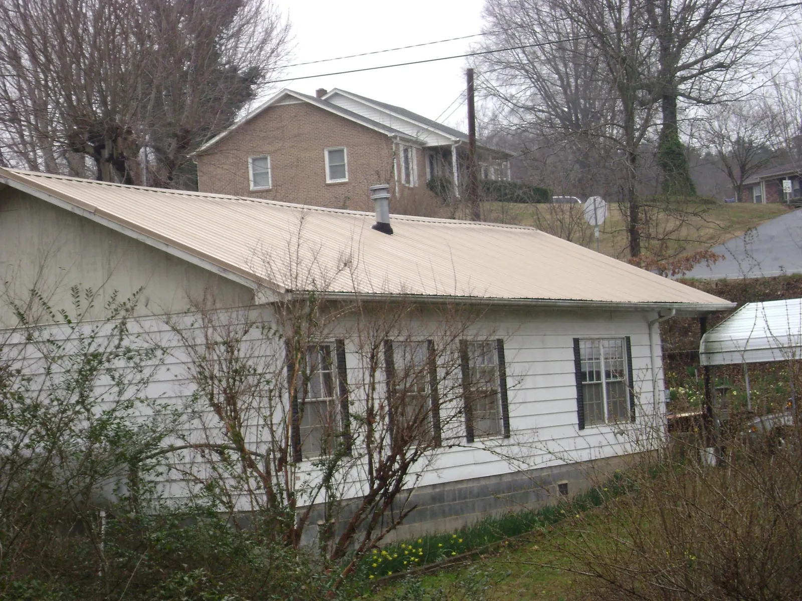 Tan metal roof on a white sided house set into a hillside — Commercial Roofing by Roofing Brothers in Pavo