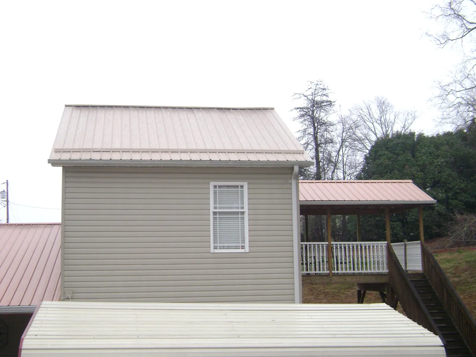 Tan metal roofs on a two story addition and attached porch, from a Roof Replacement job in Pavo